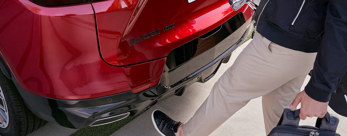 A close-up of a man using his foot to activate the hands-free liftgate on a red 2024 Chevy Blazer RS.