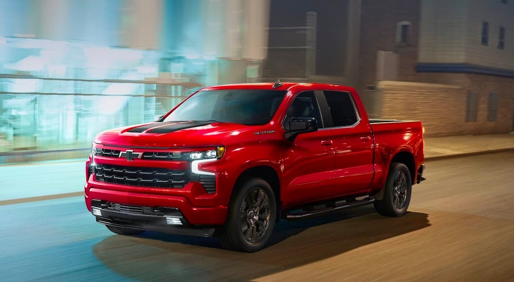 A red 2023 Chevy Silverado 1500 RST is shown driving in a city.