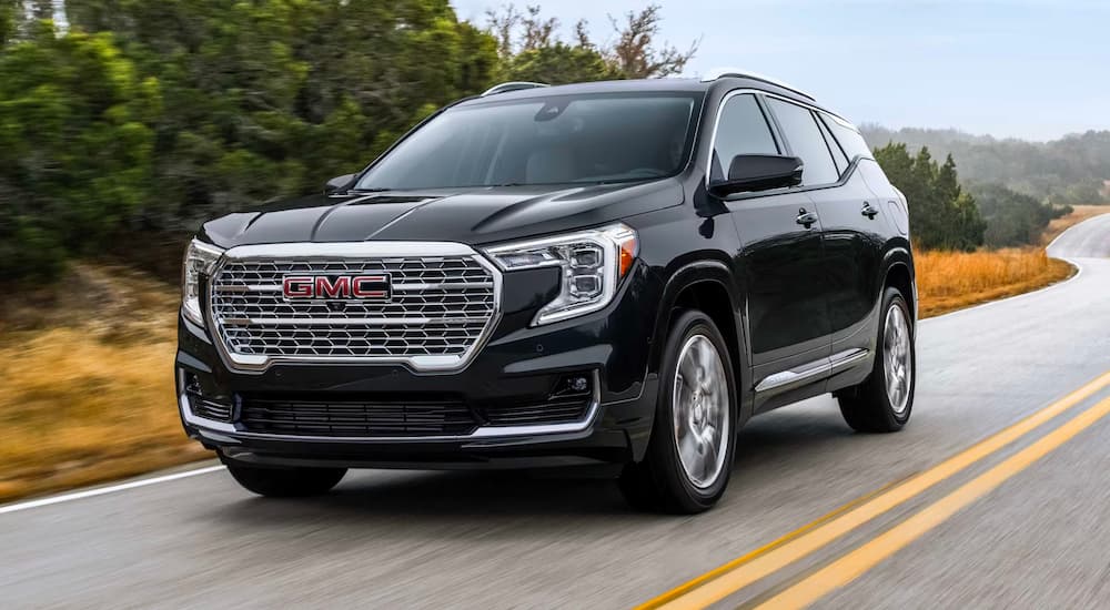 A black 2024 GMC Terrain Denali is shown driving from a GMC dealer.