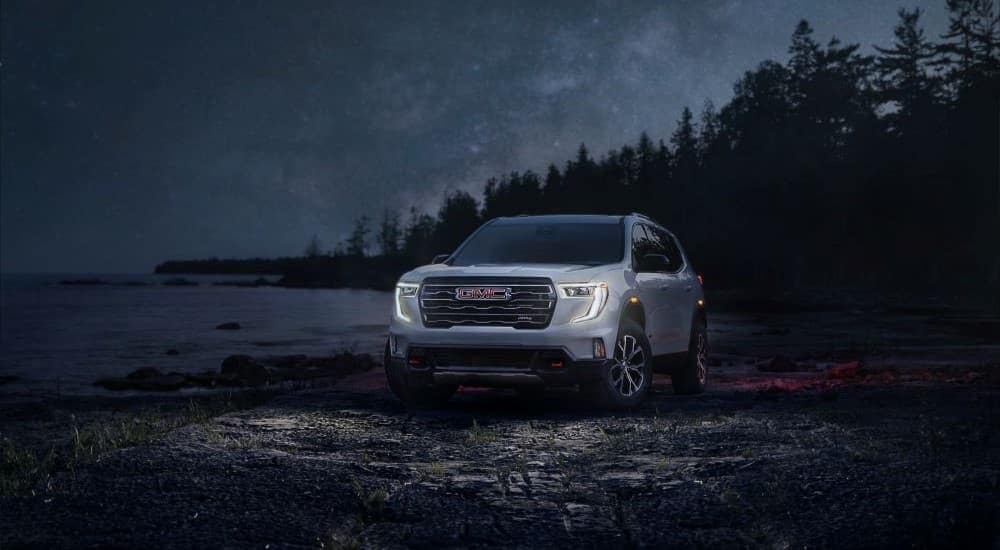 A silver 2024 GMC Acadia AT4 is shown parked on a shoreline at night.