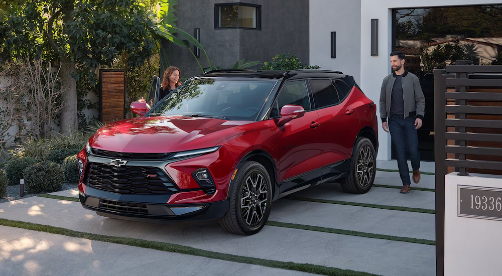 A man and woman walking to the red 2024 Chevy Blazer RS parked in their driveway.