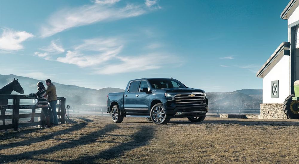 A black 2024 Chevy Silverado 1500 High Country parked near horses on a farm.