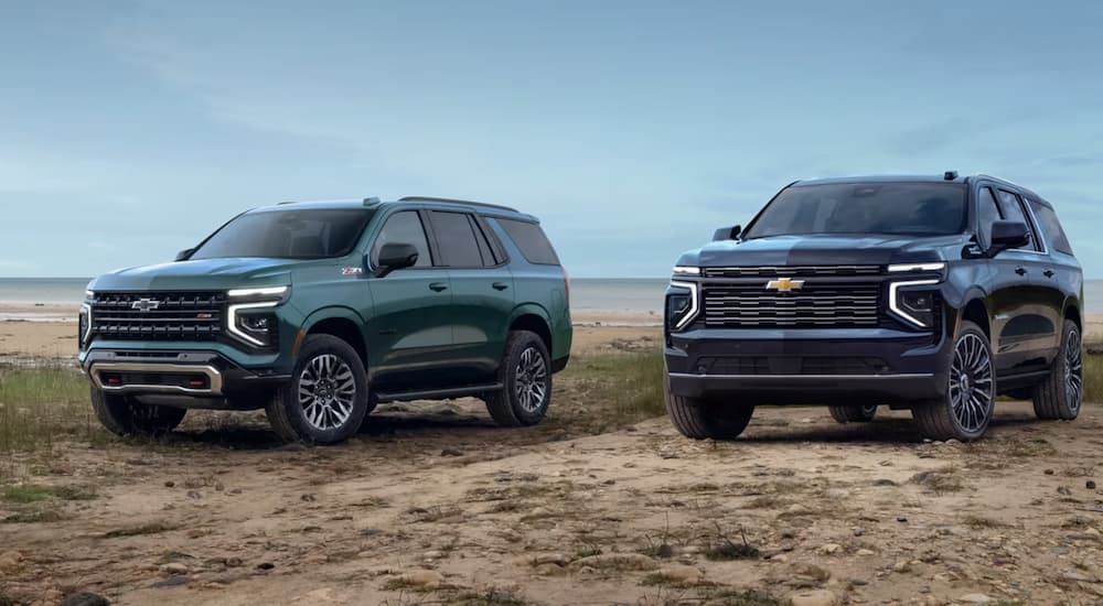 A green 2025 Chevy Tahoe Z71 and blue 2025 Chevy Suburban High Country parked on a beach.