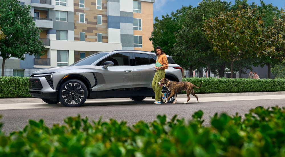 A side angle view of a woman walking by a parked grey 2025 Chevy Blazer EV.