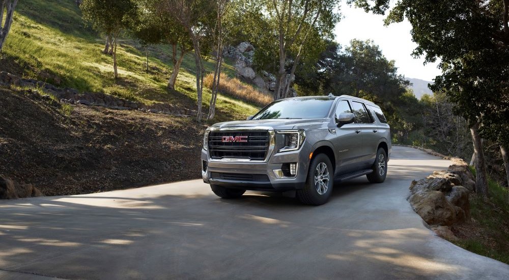 A silver 2021 GMC Yukon driving to a used car dealership.