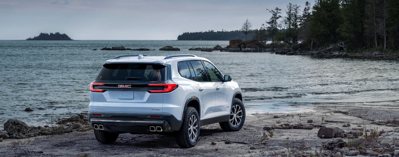 A white 2024 GMC Acadia AT4 is parked on a shore.