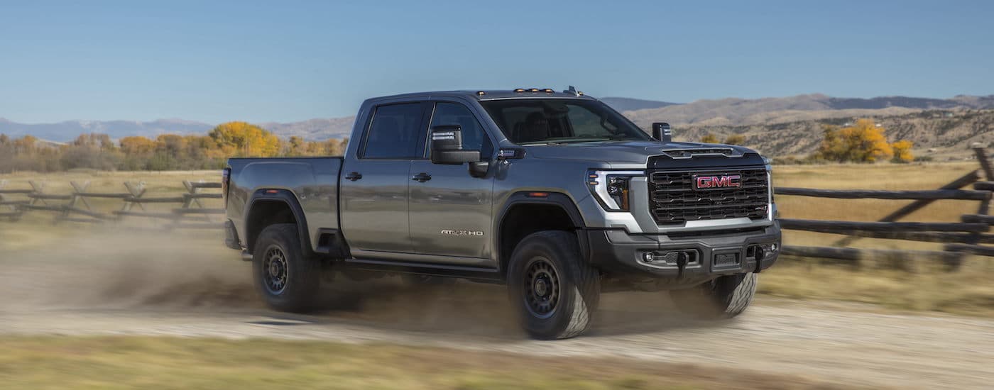 A grey 2024 GMC Sierra 2500 HD AT4x AEV is shown from the side on a dirt trail.