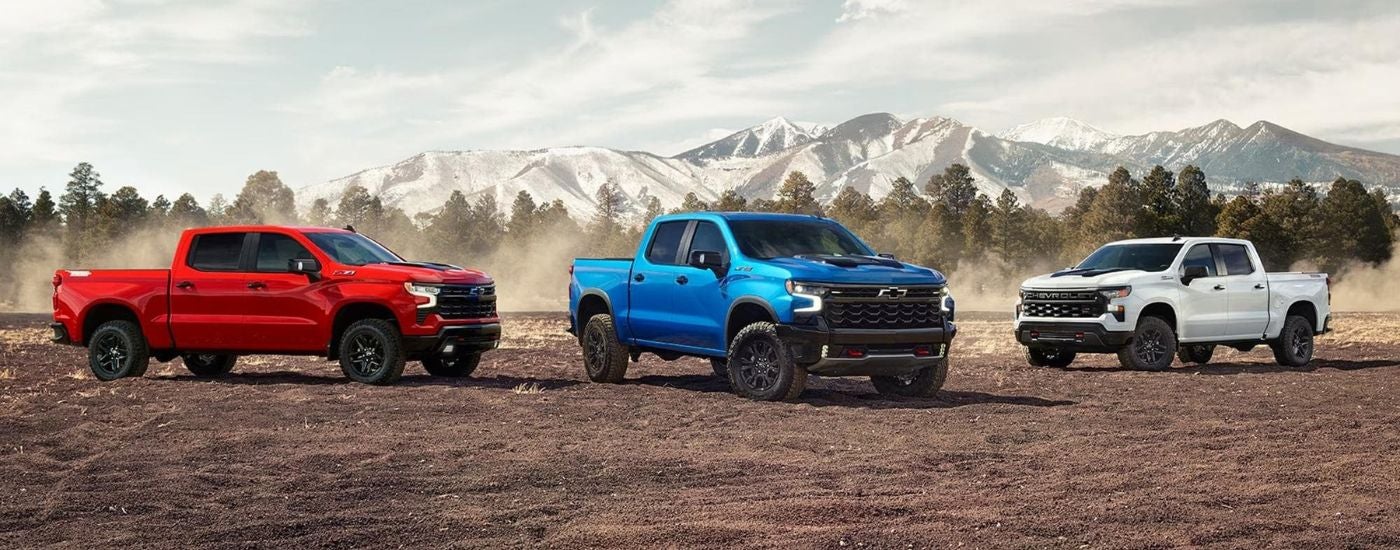 A trio of 2026 Chevy Silverado 1500s in red, white and blue with a mountain in the background.