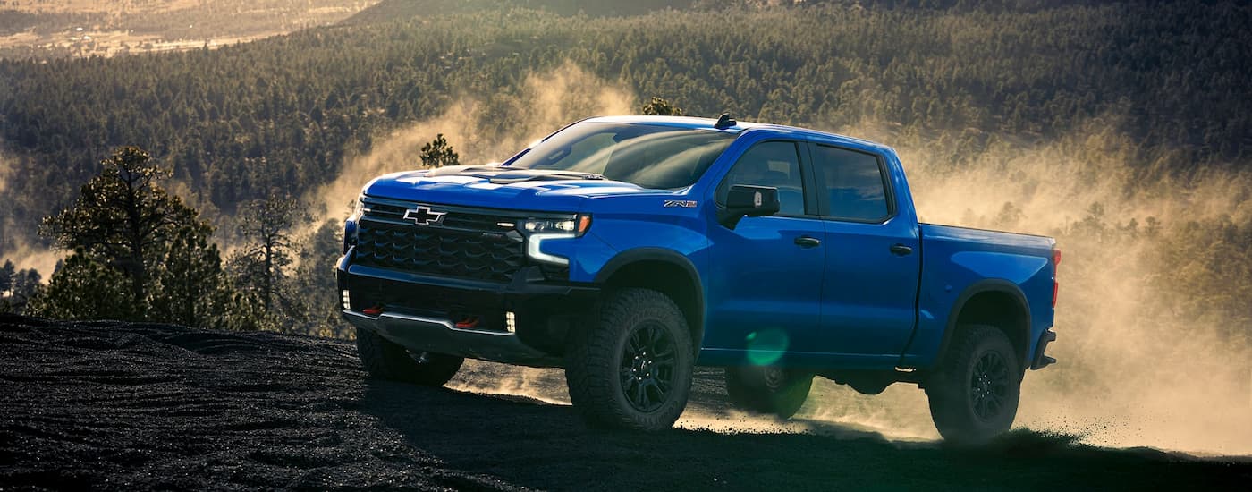 Blue 2026 Chevy Silverado 1500 ZR2 driving off-road up a hill.