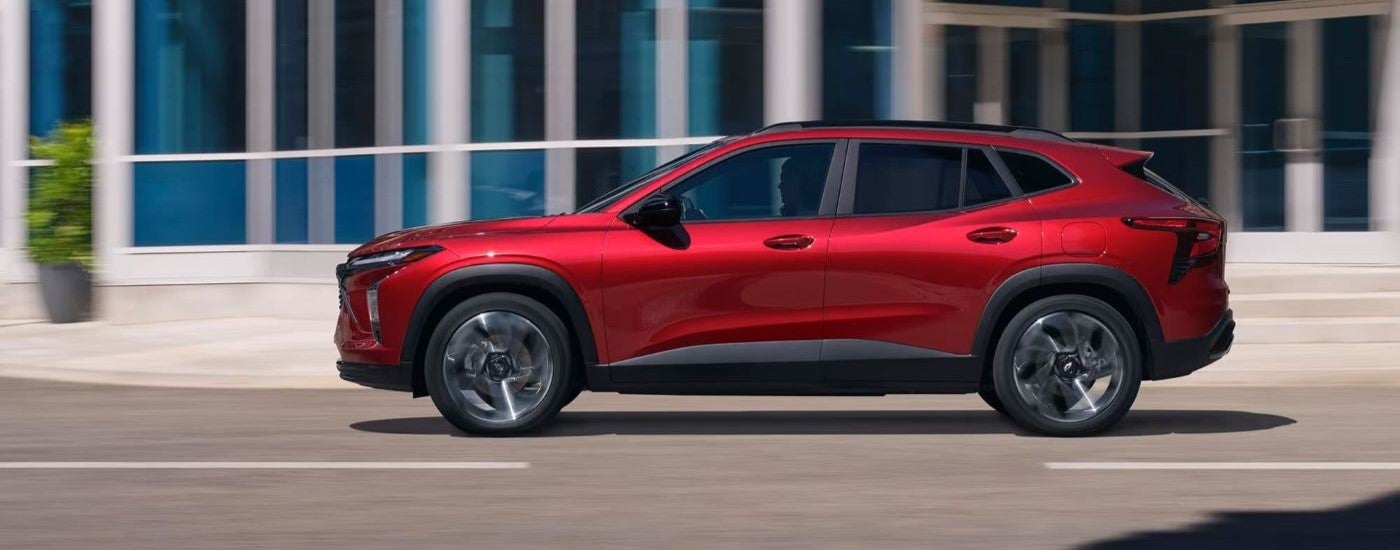 Side of a red 2026 Chevy Trax driving down a city street.