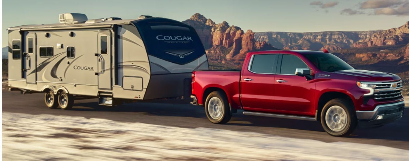 A red 2026 Chevy Silverado 1500 LTZ Z71 is towing a camper.