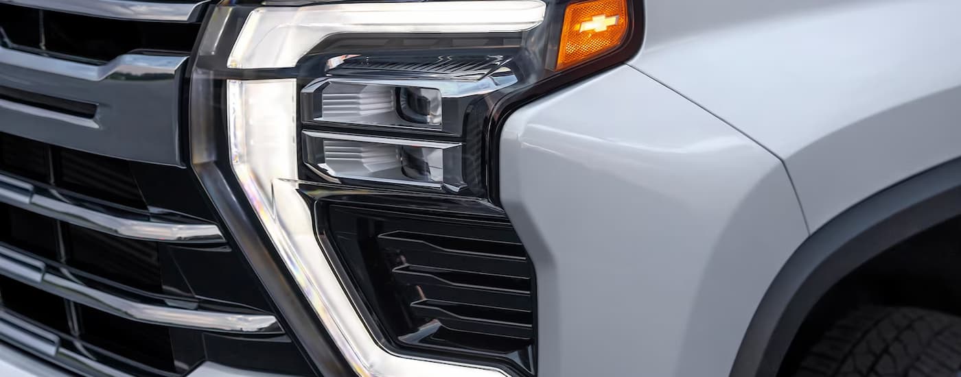 A close up shows the driver side headlight on a white 2024 Chevy Silverado 3500 HD LTZ after leaving a Chevy dealer.