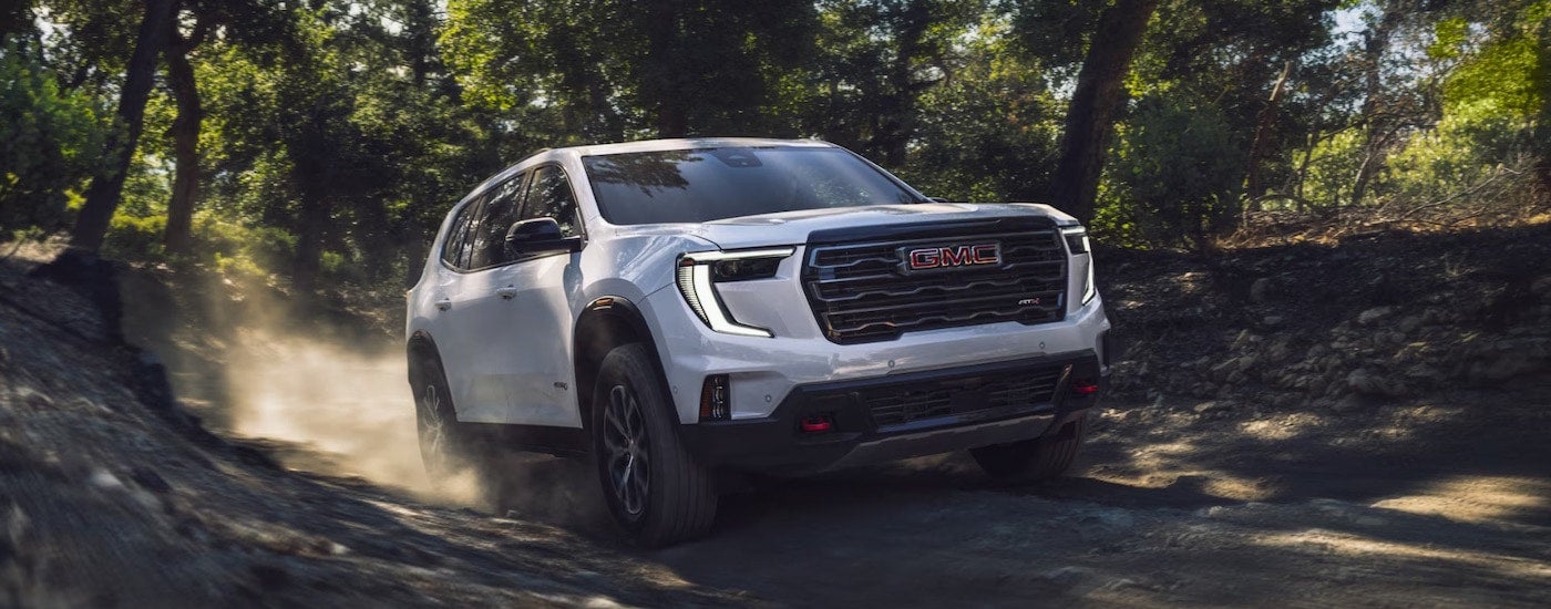 A white 2024 GMC Acadia AT4 is driving on a trail.