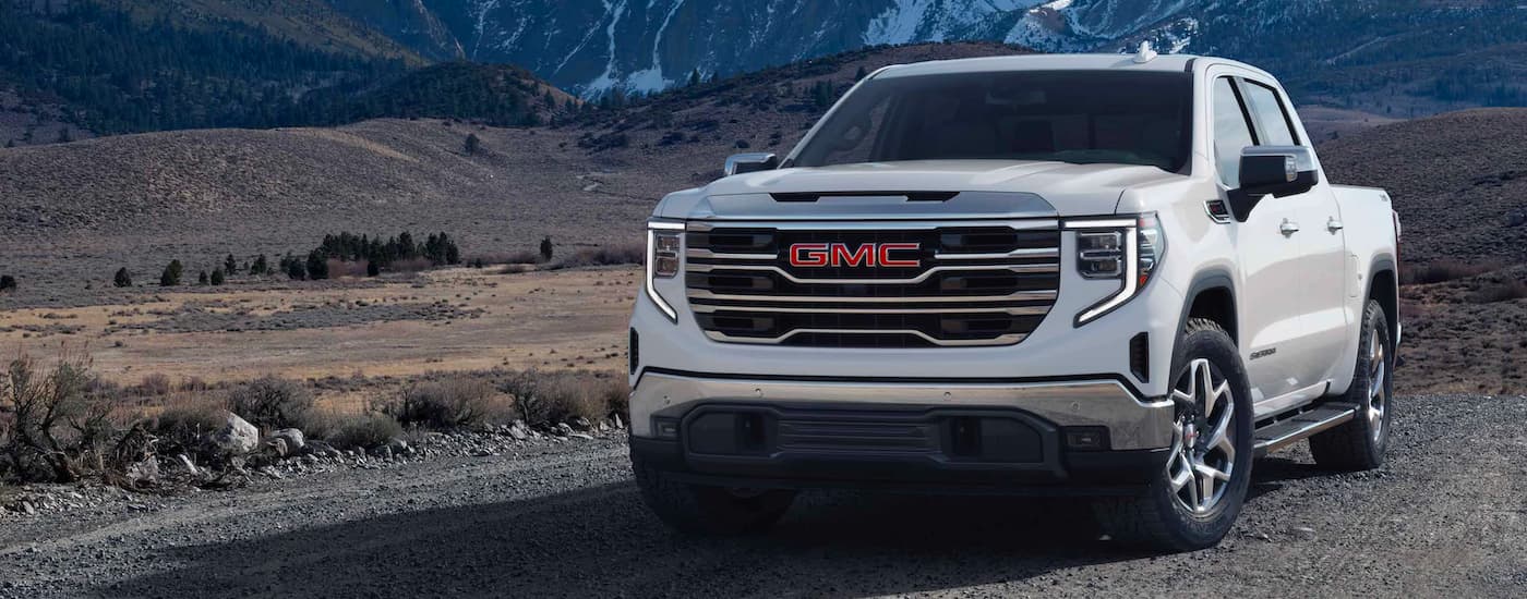 White 2023 GMC Sierra 1500 driving off-road from a used car dealership.