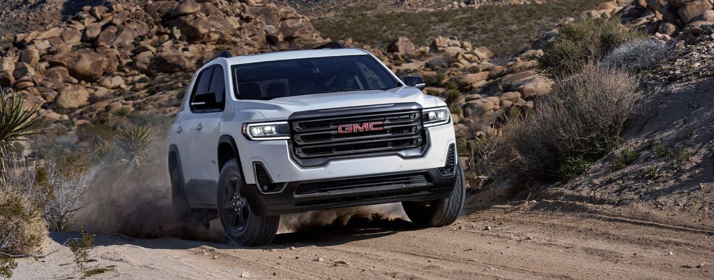 A white 2022 GMC Acadia driving toa used GMC dealer.