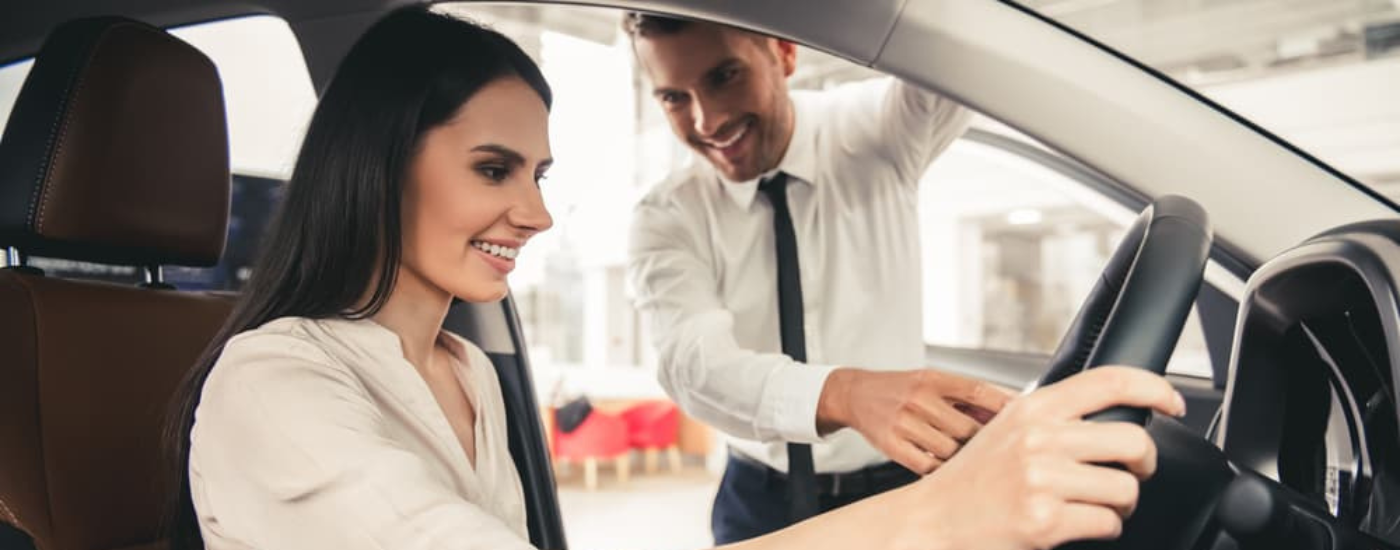 A woman inside a vehicle speaking to a salesman